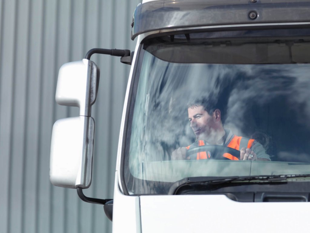 A lorry driver seen through the windscreen of his cab.