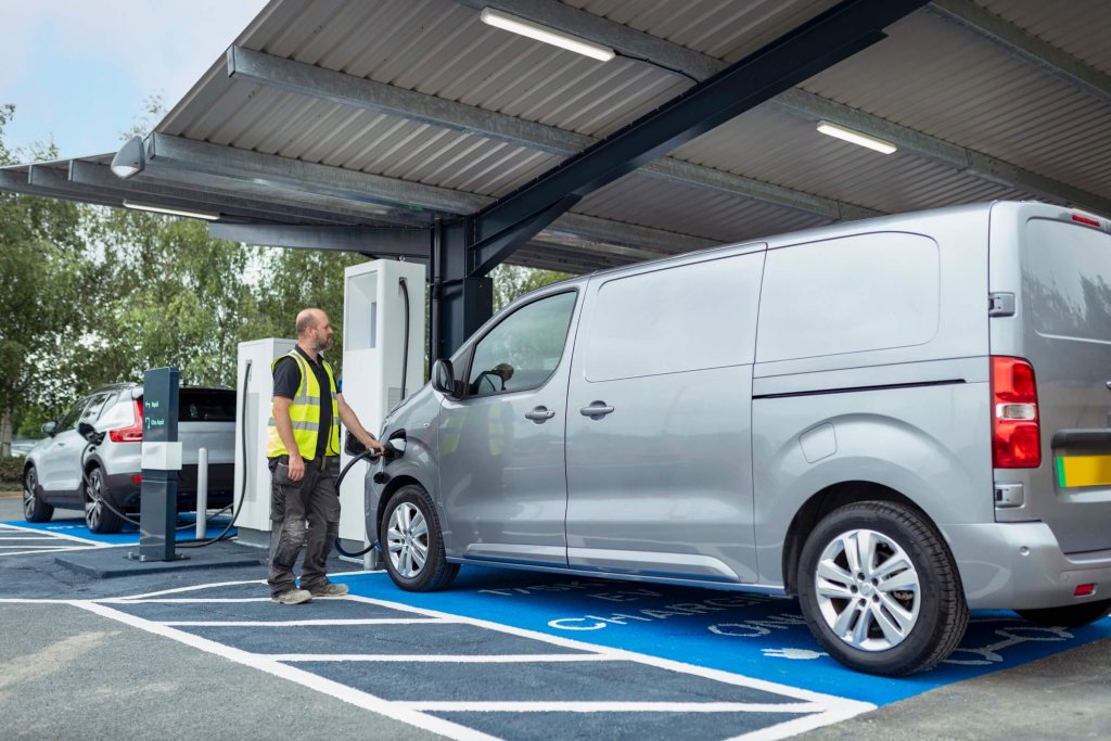 A grey electric van charging at a bay in a charging area.