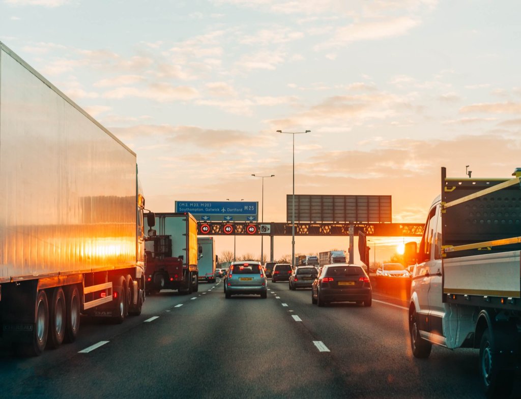 Lorries on a motorway at sunset beside an overhead gantry.