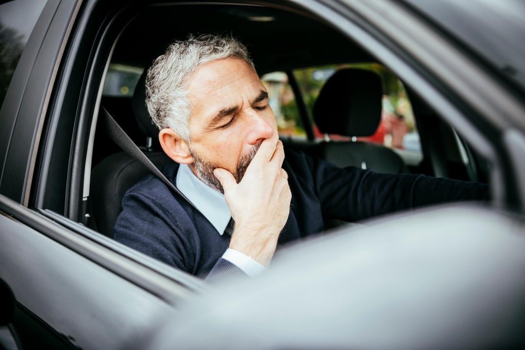 A tired driver yawning at the wheel of a car.