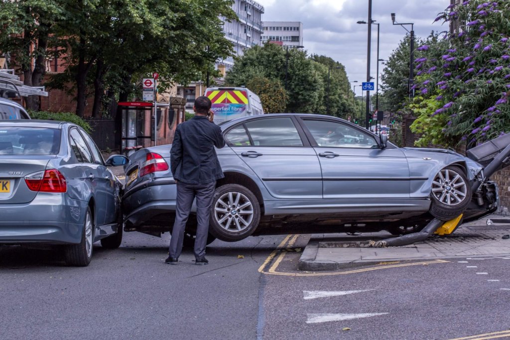 A damaged car stopped on a street after an accident, with a man standing beside it.