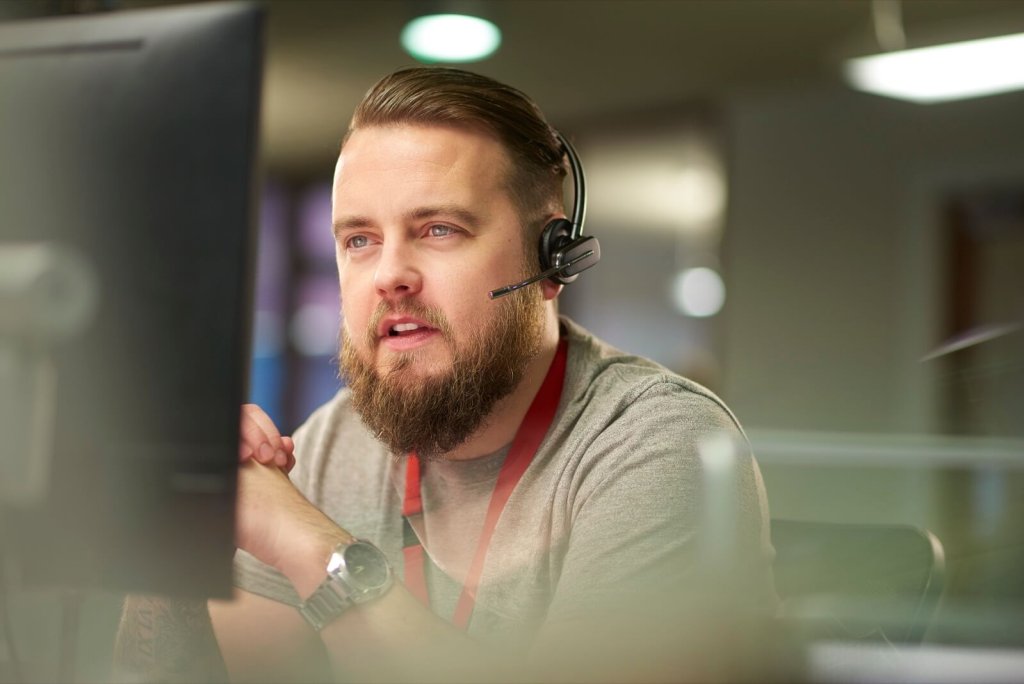 A man wearing a headset working at a computer in a control room.