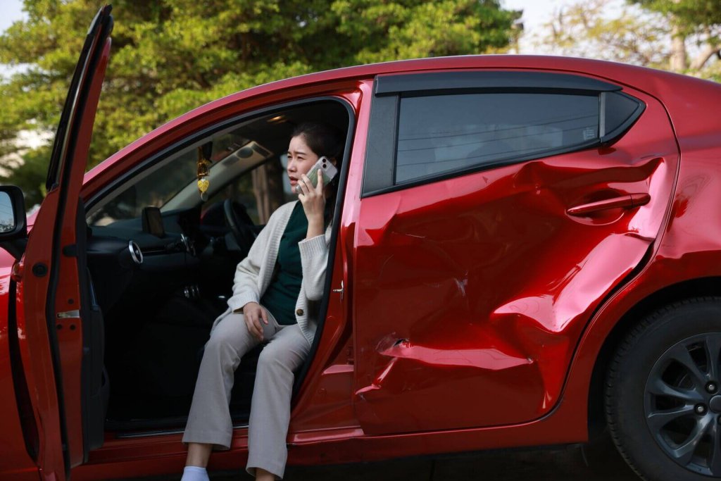 Driver on the phone sitting in her damaged red car after a collision.