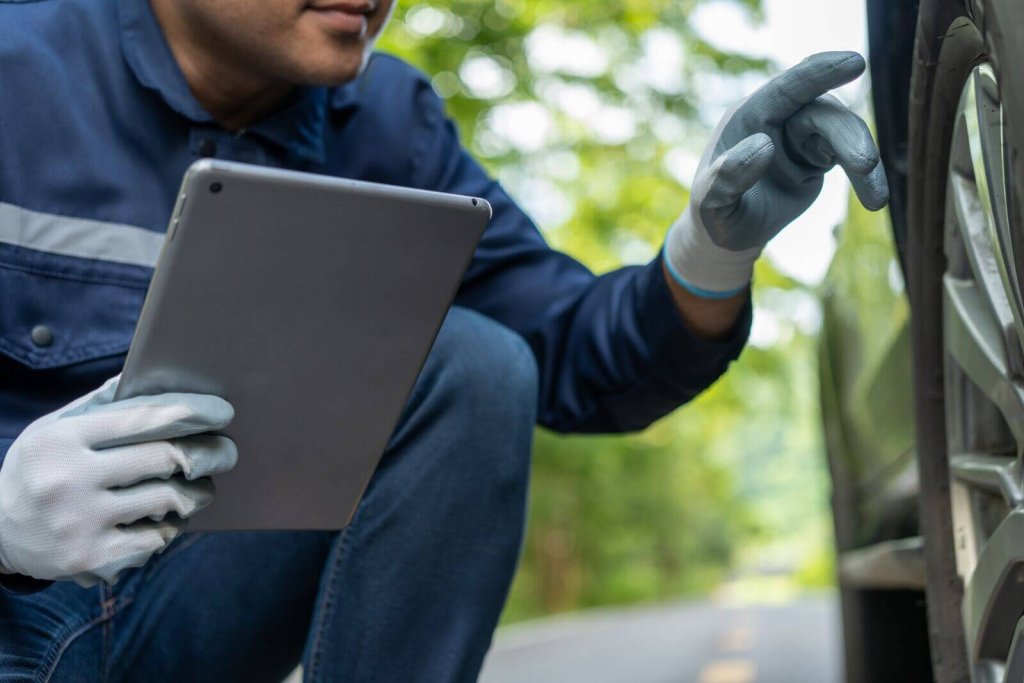 Technician in gloves inspecting a vehicle wheel with a tablet.
