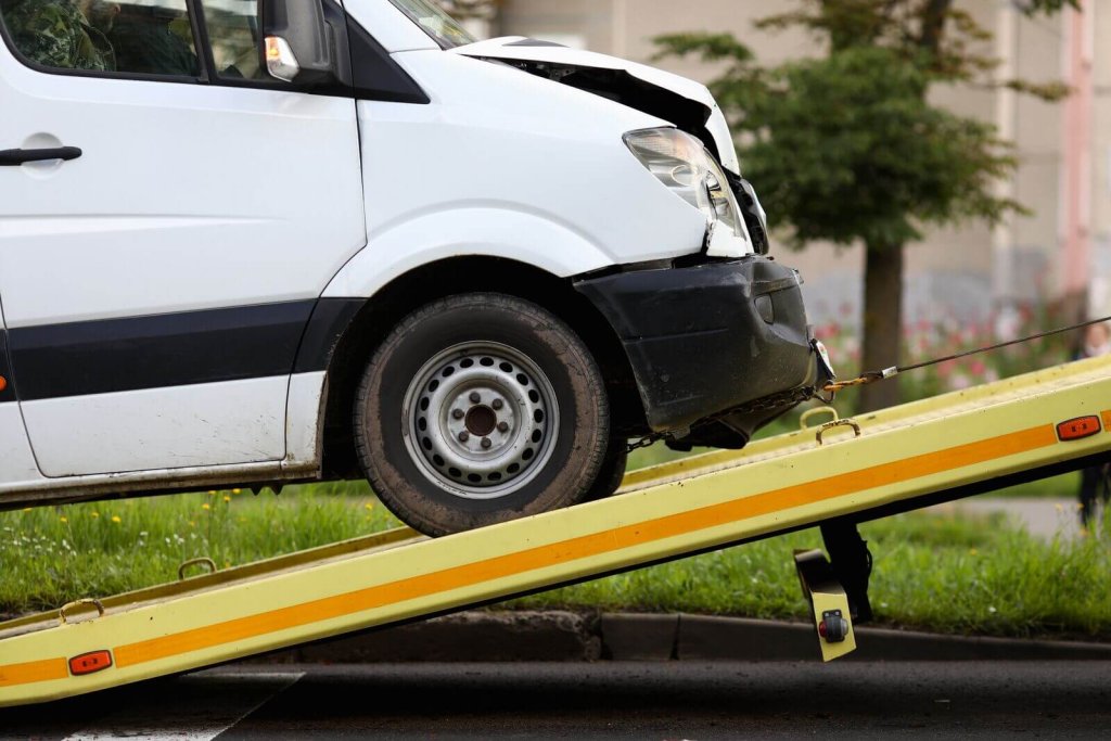 Damaged white van being loaded onto a recovery vehicle ramp.