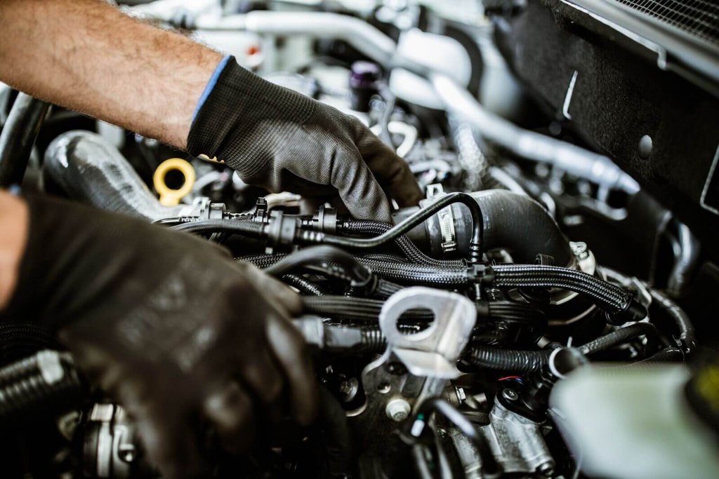 Technician in gloves working on a vehicle engine.