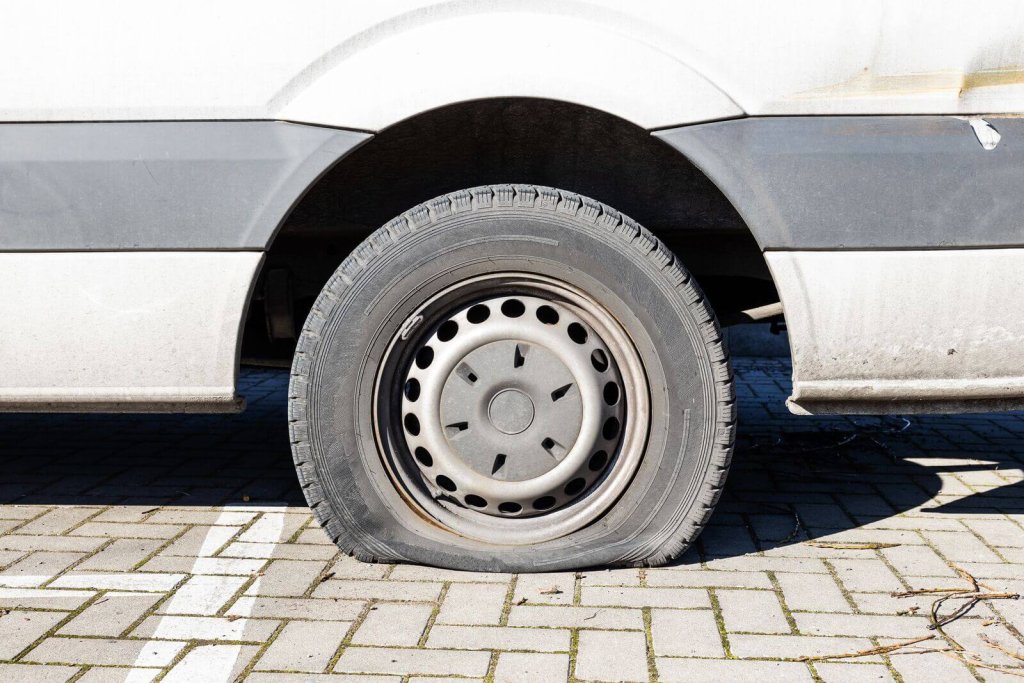 White van with a flat tyre parked on block paving.