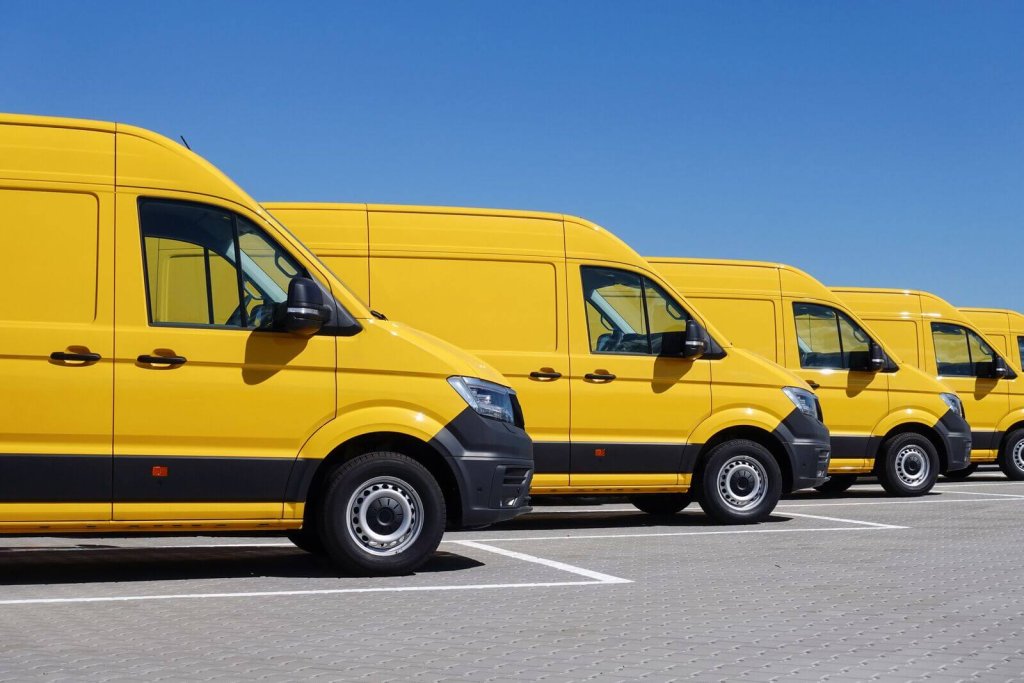 Row of yellow fleet vans parked in a car park.