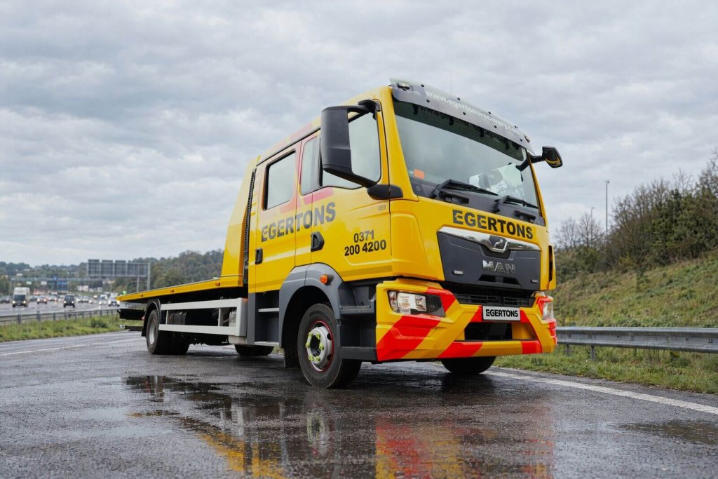 Egertons yellow flatbed recovery truck on a wet motorway at dusk.