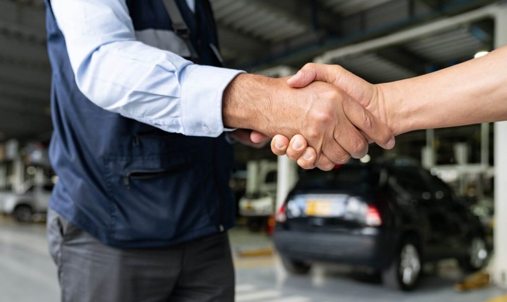 Two business partners shaking hands in a vehicle workshop.